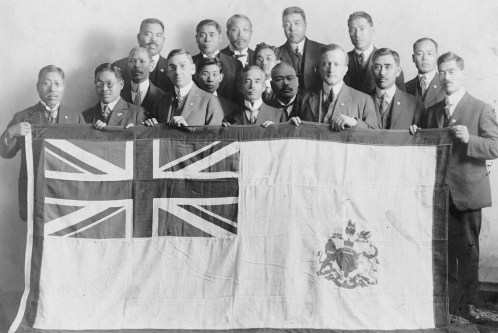 Commemorative photograph taken at the end of the war, circa 1918. Matsunoshin Abe, the president of the Canadian Japanese Association at the time, is the man on the far left, and Saburo Shinobu is on the far right. Consul General Satotsuga Ukita, who was in office 1916-1921, is in the centre of the front row (fourth from the left holding the flag). NNM 1994.70.27.
